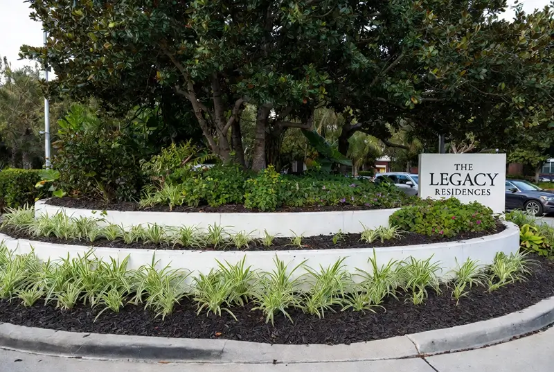 Before The Legacy Residences Entrance With Purple Flowers And Trimmed Tree